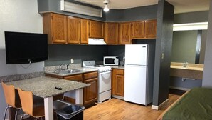 A compact kitchen with wooden cabinets, a microwave, a refrigerator, and a small dining area with chairs.