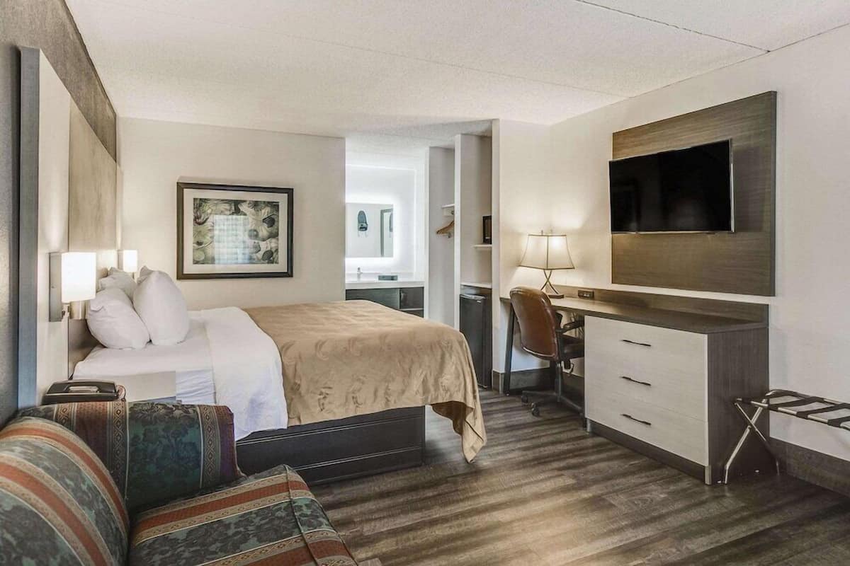 A hotel room with a bed, a desk, a chair, a TV, and a framed picture on the wall.