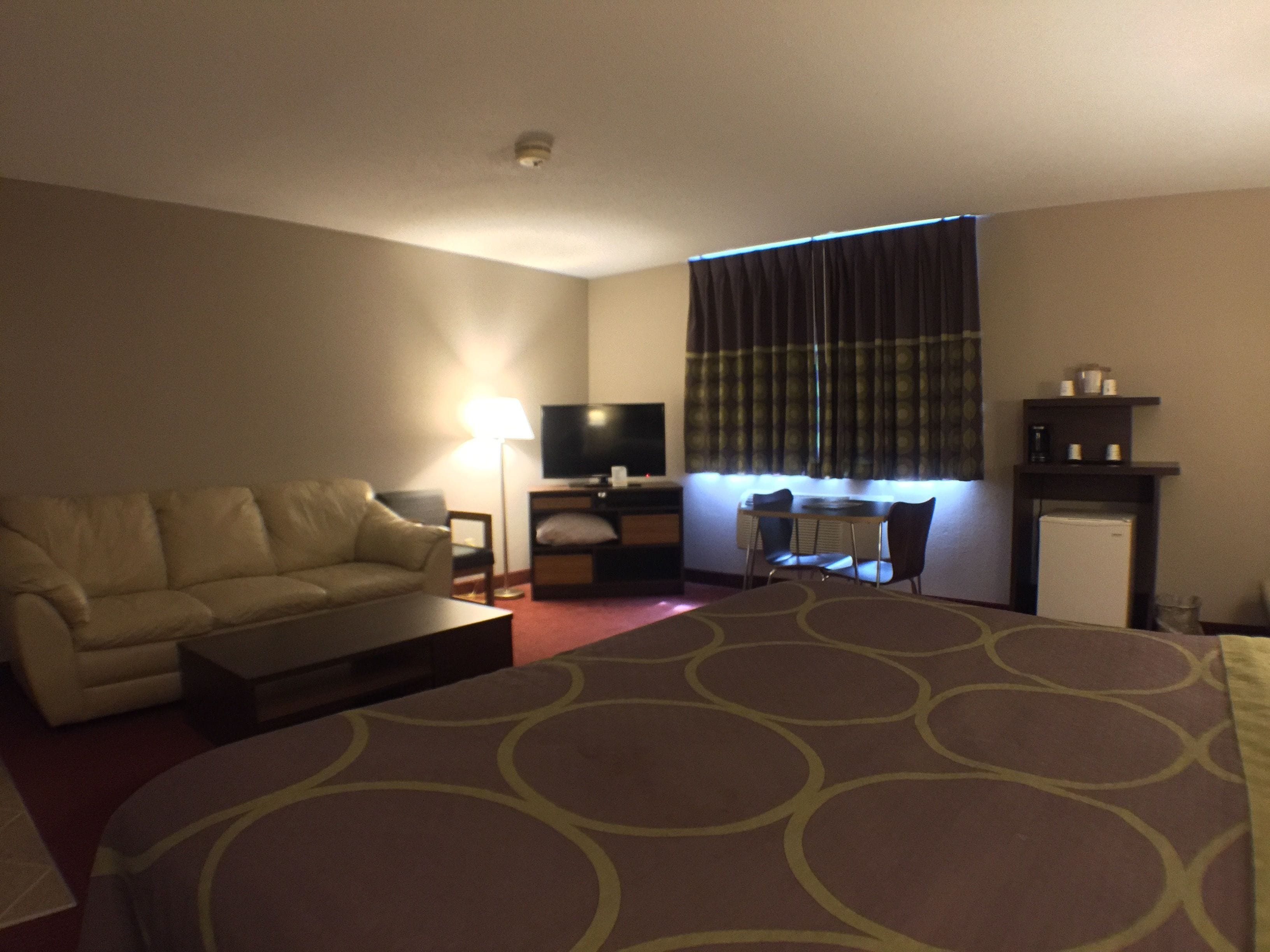 A hotel room with a sofa, a small table, a TV, a desk with a chair, and a refrigerator.