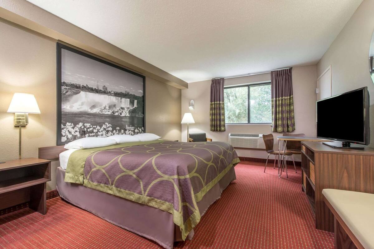 Ein Hotelzimmer mit Bett, Schreibtisch, Fernseher und einem großen Fenster.