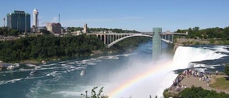 A waterfall with a rainbow, a bridge, and a cityscape in the background.