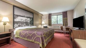 Quarto de hotel com cama, escrivaninha, televisão e uma janela grande.