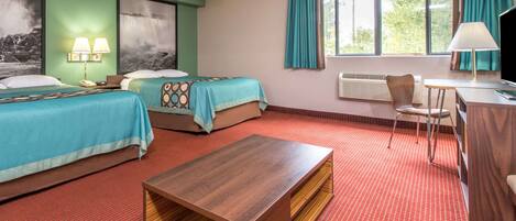 A hotel room with two beds, a wooden coffee table, a desk with a chair, and a window with curtains.