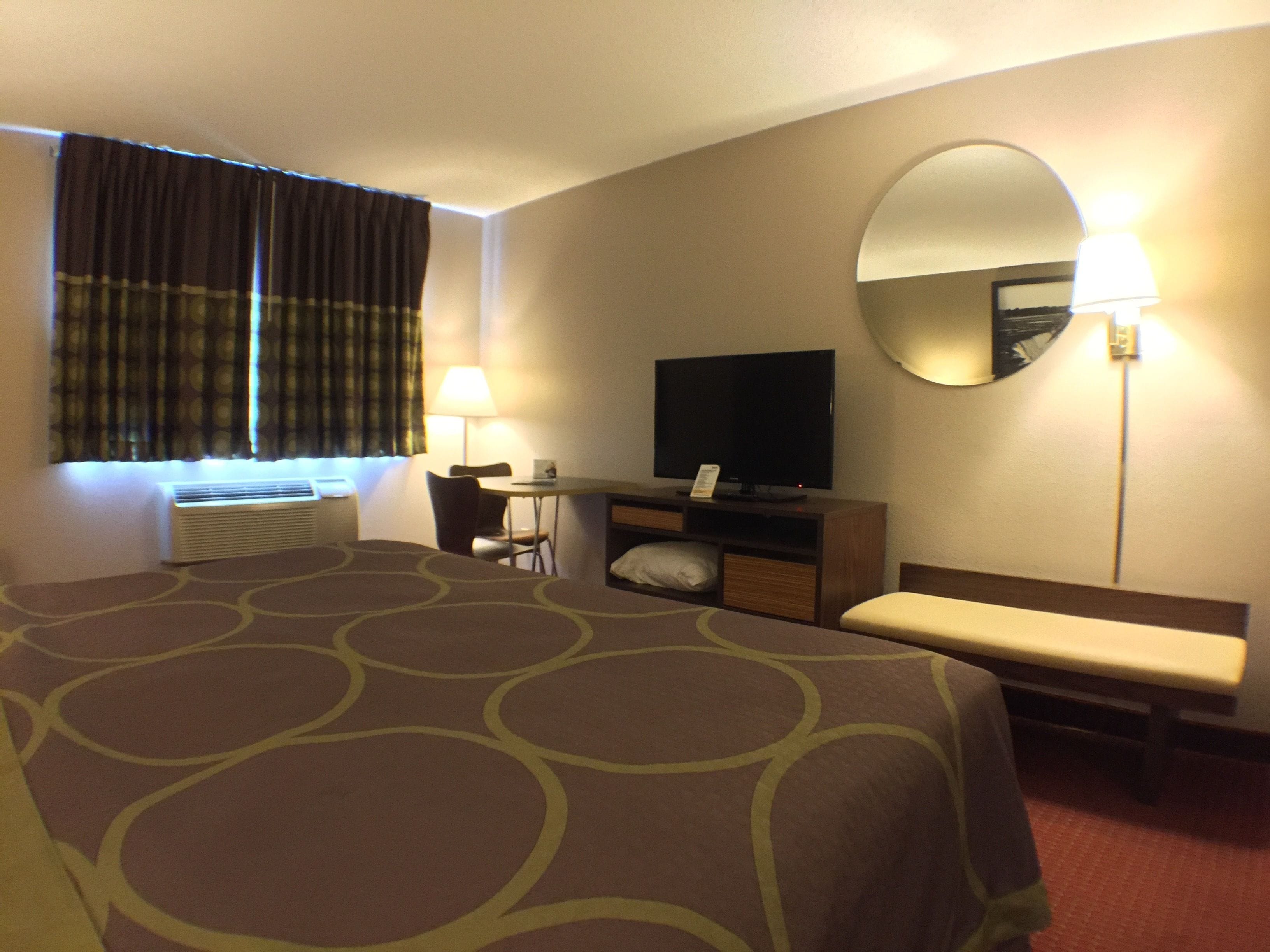 A hotel room with a large bed, a desk with a chair, a television, a mirror, and a window with curtains.
