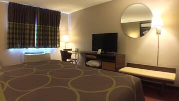 A hotel room with a large bed, a desk with a chair, a television, a mirror, and a window with curtains.