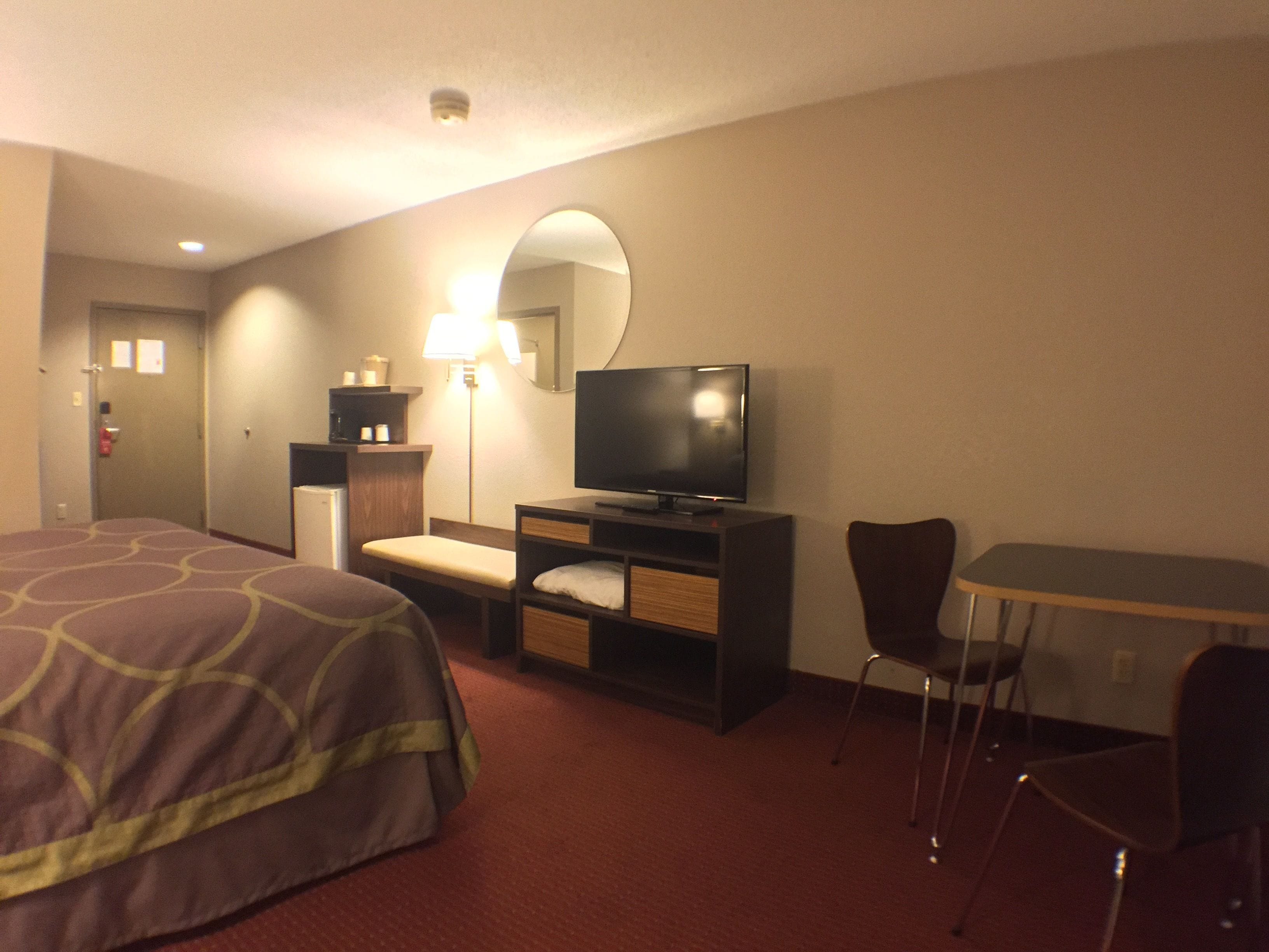 A hotel room with a bed, a desk with a television, a chair, and a lamp.