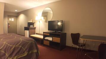 A hotel room with a bed, a desk with a television, a chair, and a lamp.