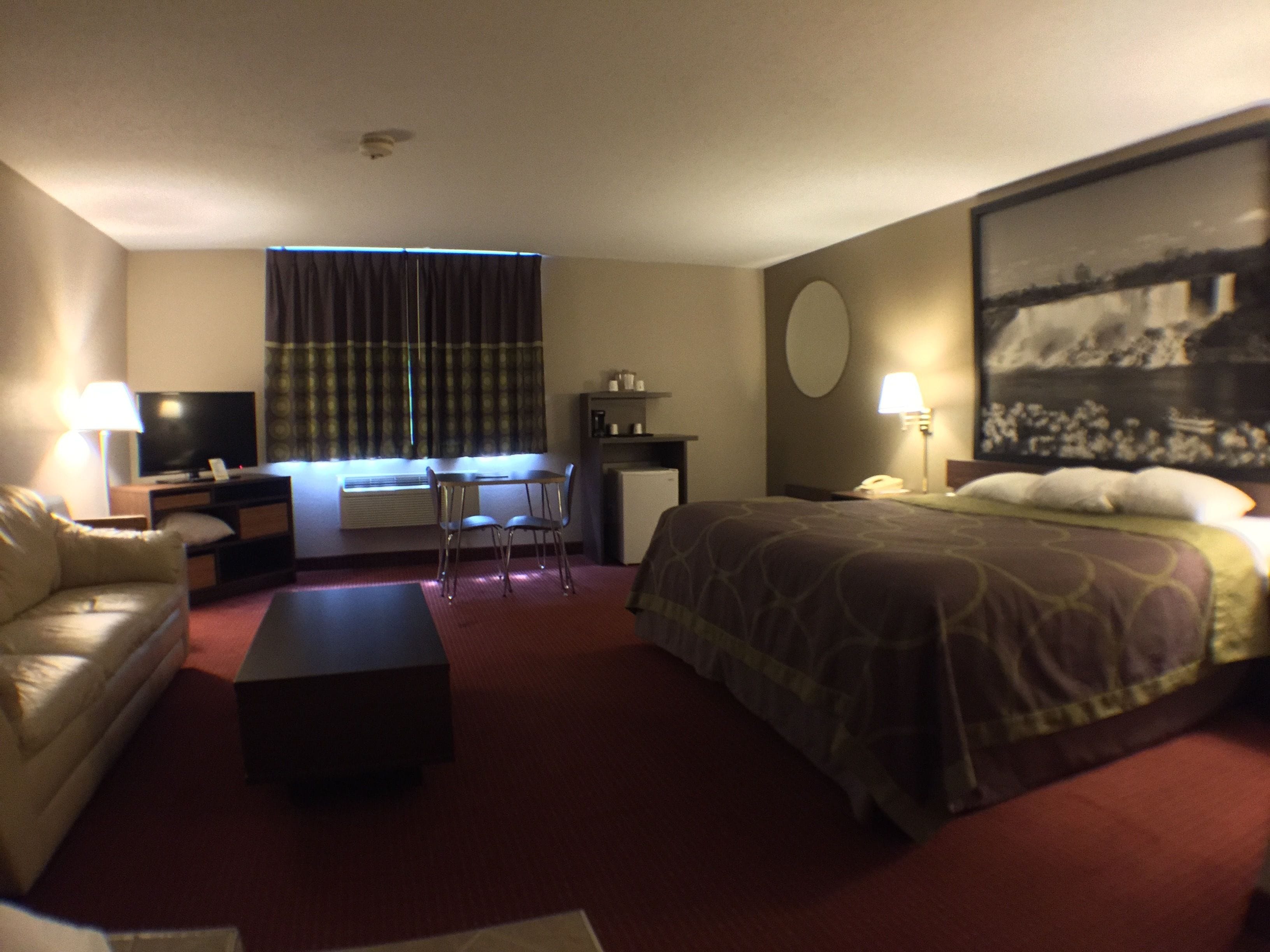 A hotel room with a bed, a desk, a chair, a sofa, a television, and a painting on the wall.