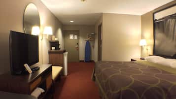 A hotel room with a bed, a desk with a computer, a mirror, a coat rack, and a door leading to a hallway.