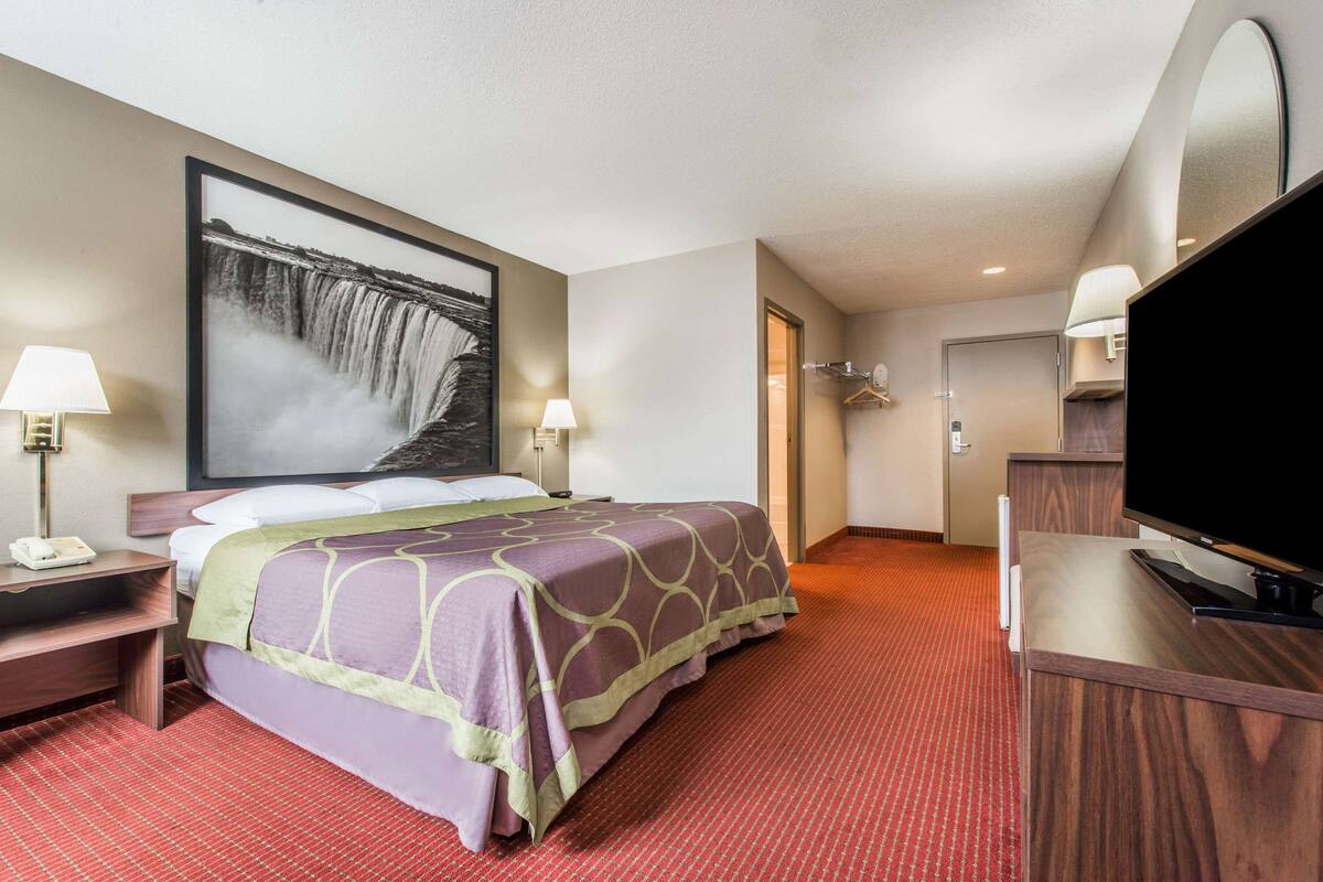 Ein Hotelzimmer mit einem Bett, einem Schreibtisch, einem Fernseher und einem großen Wandbild von einem Wasserfall.
