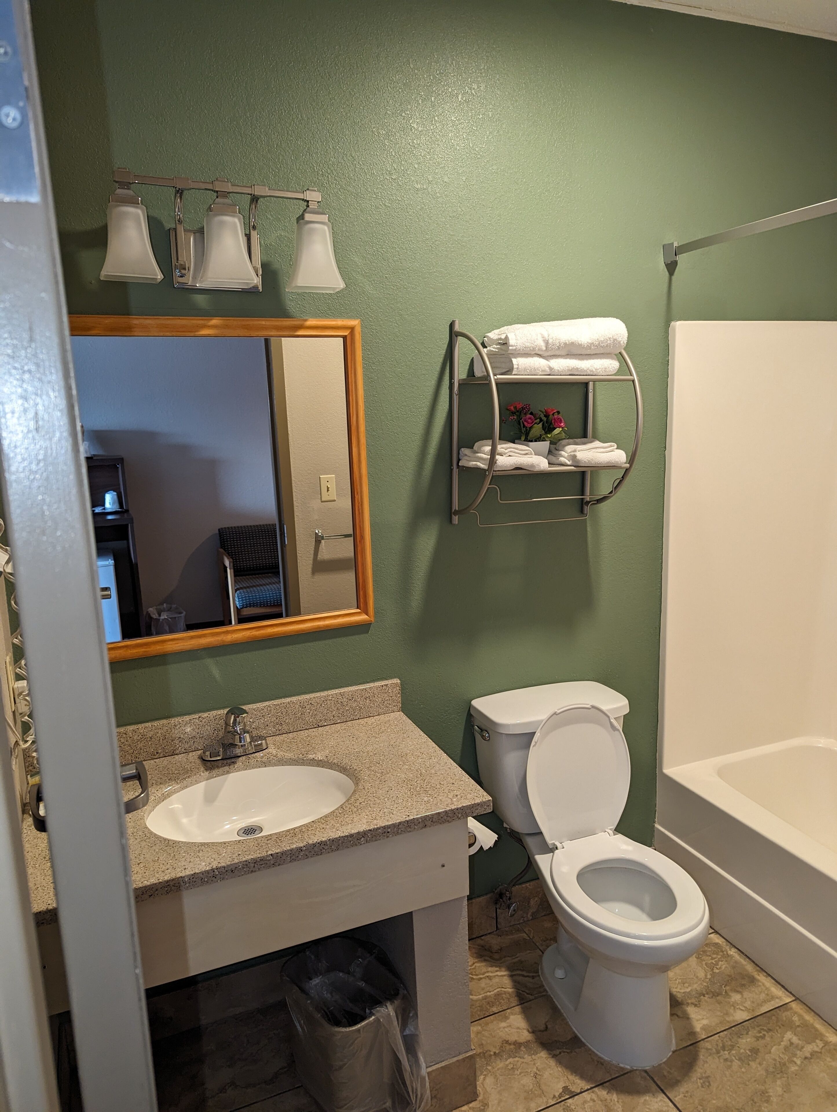 Une salle de bain équipée d’un lavabo, de toilettes et d’une baignoire. On y trouve un porte-serviettes avec des serviettes et une petite étagère avec des fleurs.