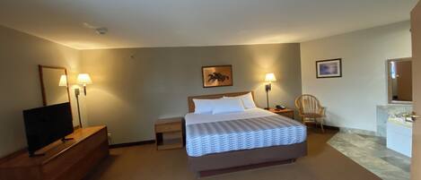 A hotel room with a bed, bedside lamps, a chair, a desk with a TV, and a bathroom with a mirror.