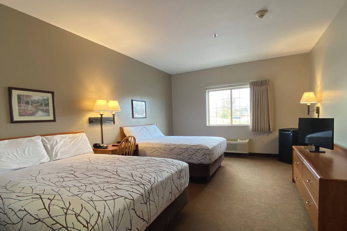 A hotel room with two beds, a desk, a chair, a TV, and a window with curtains.