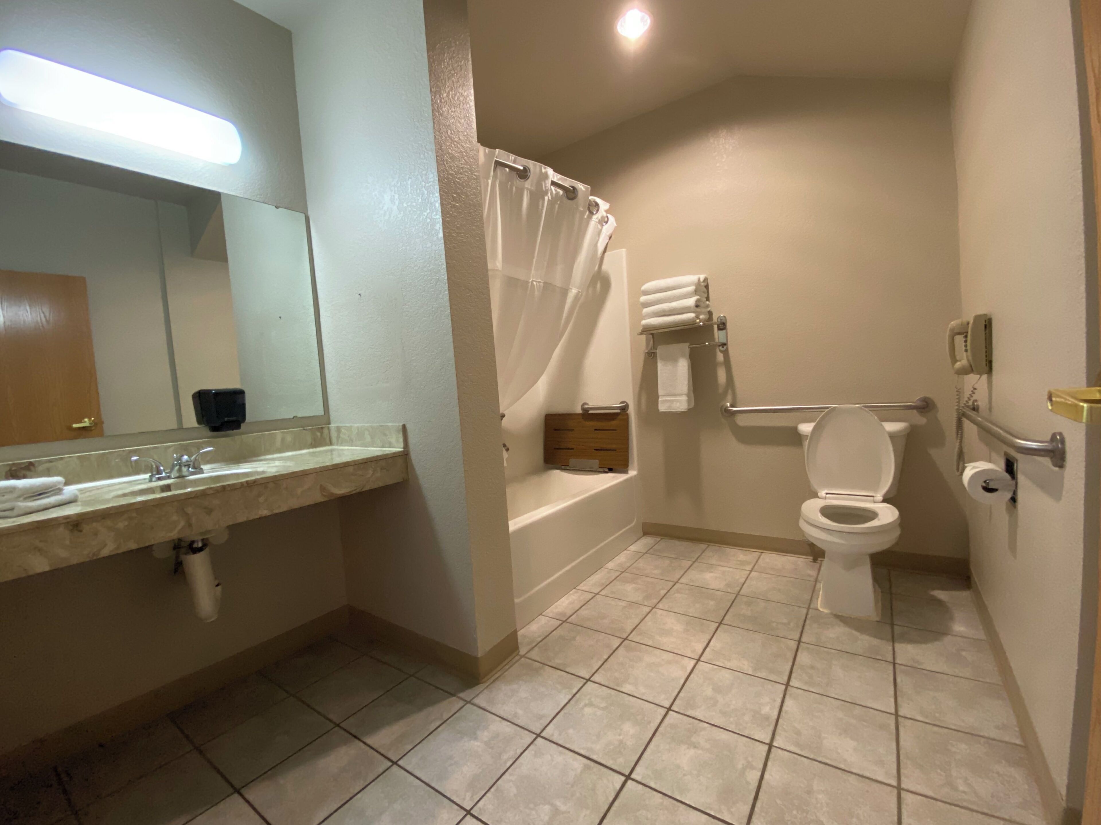 A bathroom with a sink, mirror, toilet, shower, and a handrail.