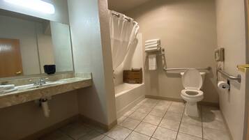 A bathroom with a sink, mirror, toilet, shower, and a handrail.
