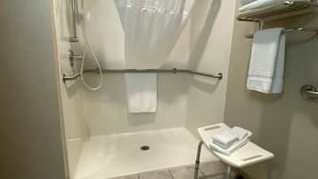 A shower with a white curtain, a small step stool, and a towel rack with folded towels.
