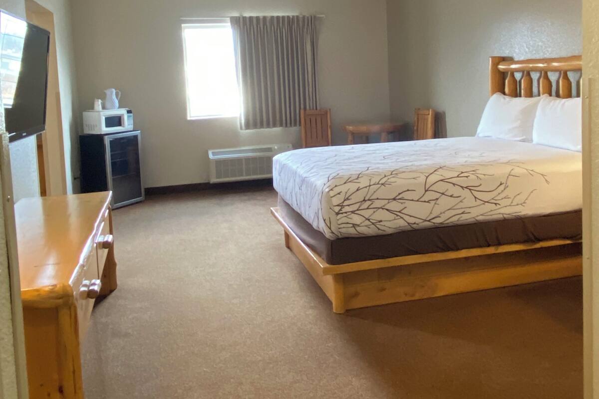 A hotel room with a bed, a desk, a television, and a window with curtains.