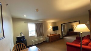 Une chambre d’hôtel avec une table en bois, un canapé rouge, une télévision, une fenêtre avec des rideaux, un radiateur et une lampe.