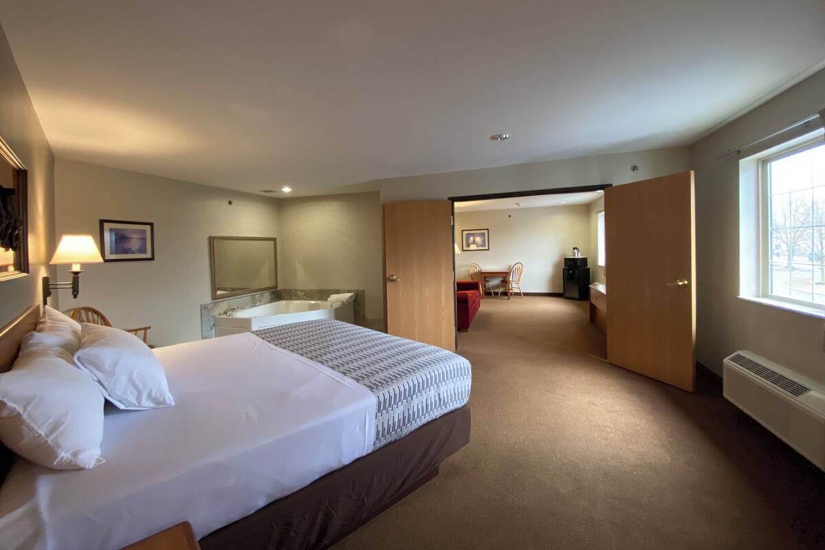A hotel room with a bed, a desk, a chair, a bathroom with a bathtub, and a window.