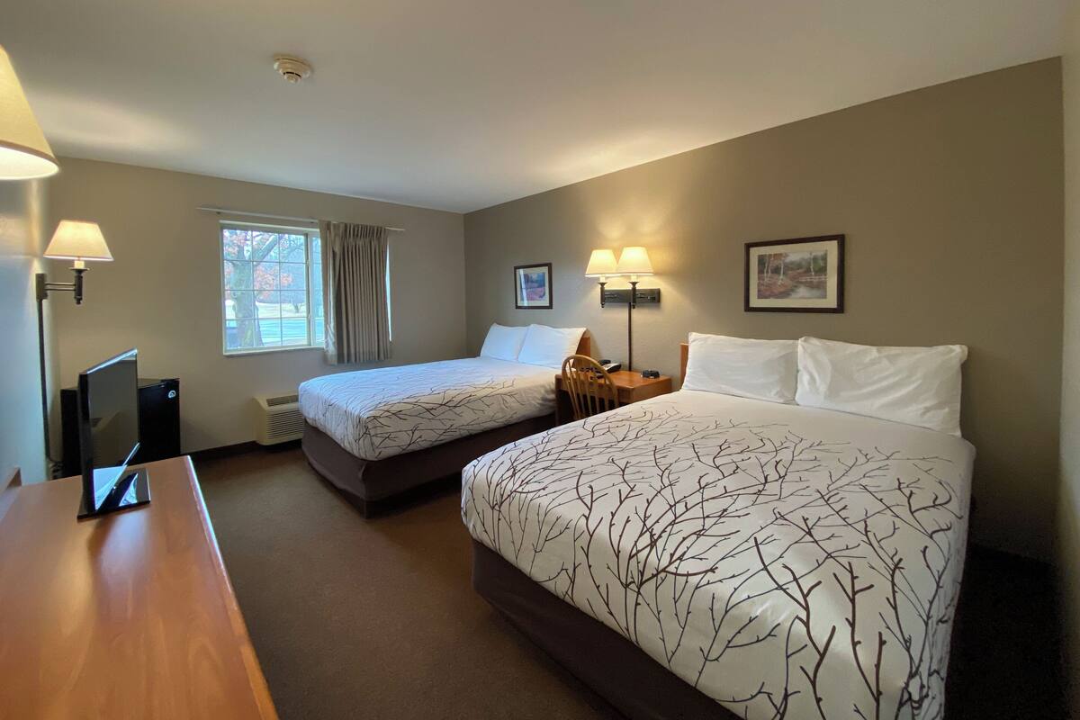 A hotel room with two beds, a desk, a chair, a TV, and a window with curtains.