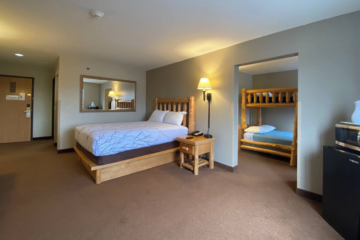 A hotel room with a single bed, a bedside table with a lamp, a mirror, and a bunk bed.