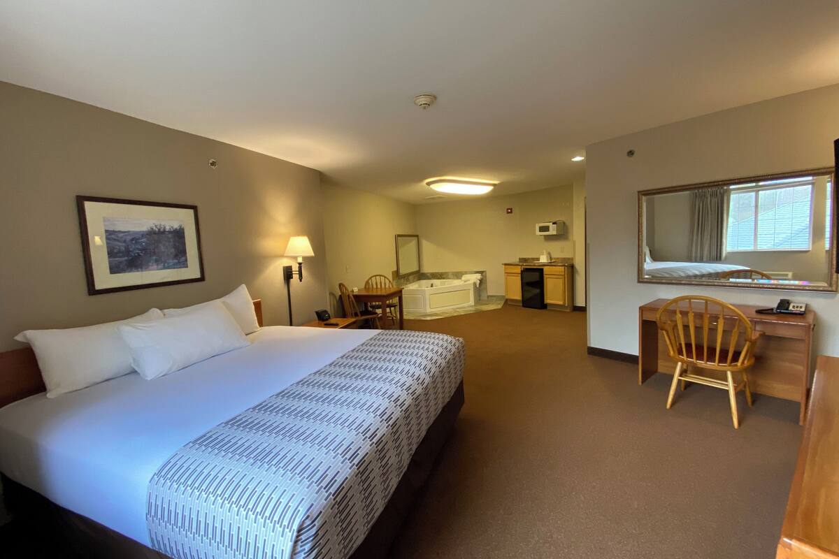 A hotel room with a bed, desk, chair, and a bathroom with a bathtub.