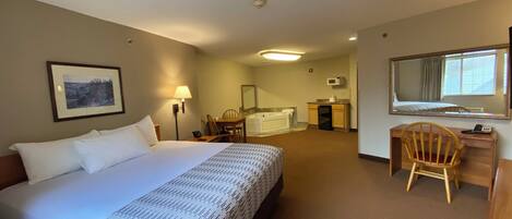 Quarto de hotel com cama, escrivaninha, cadeira e banheiro com banheira.