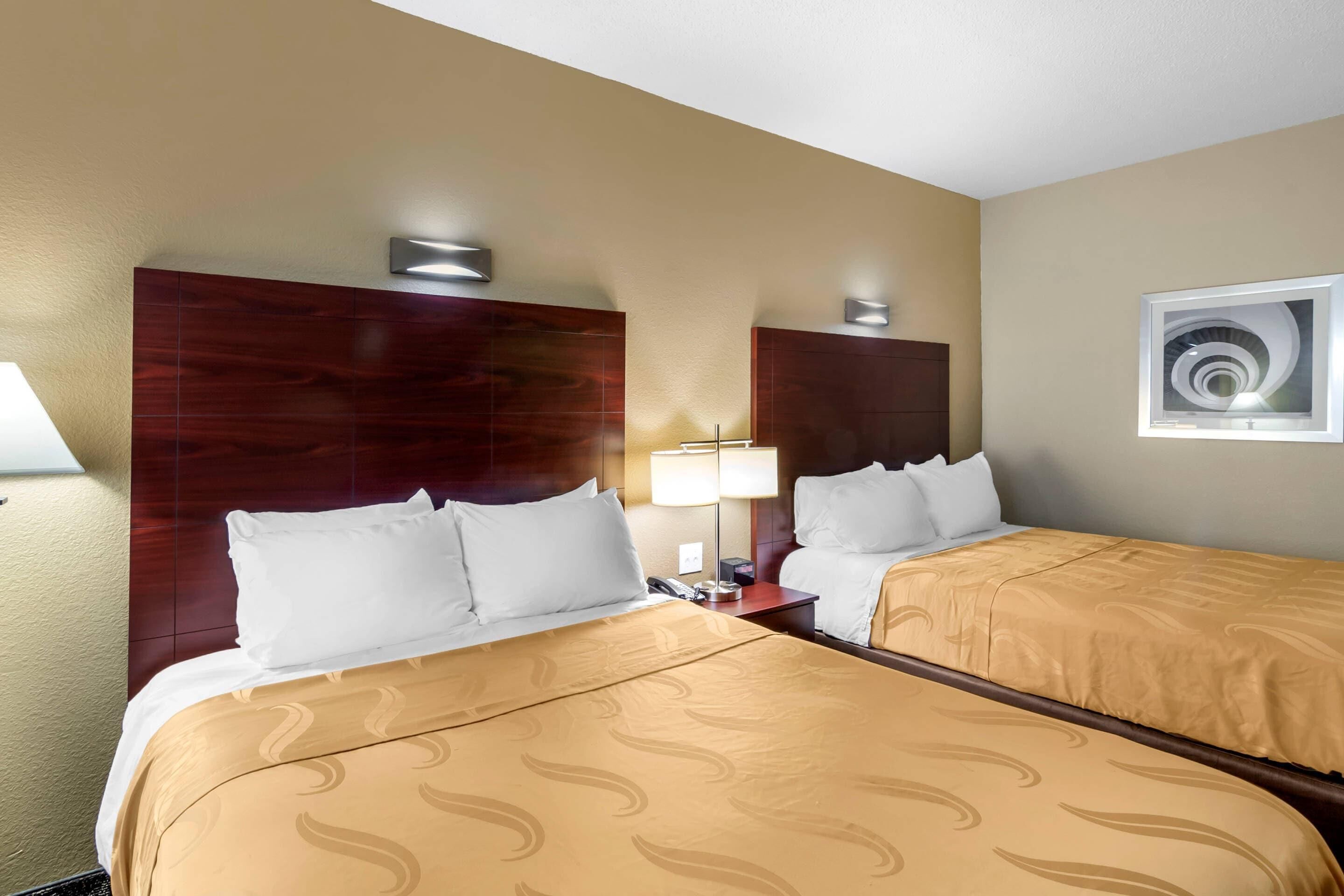 Een hotelkamer met twee bedden, houten hoofdeinden, een wandlamp, een telefoon en een lijst met een afbeelding.