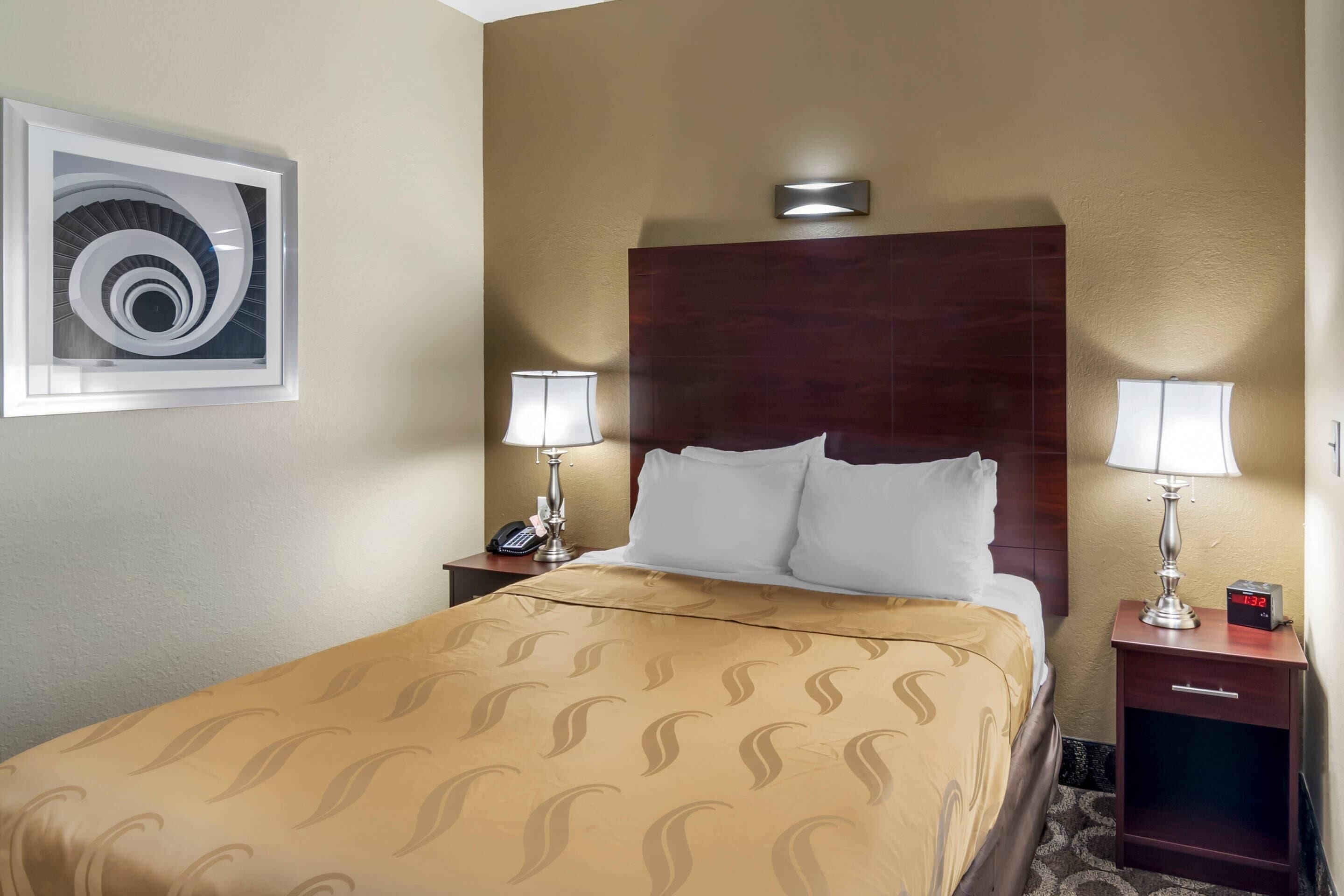 Une chambre d’hôtel avec un grand lit, deux tables de chevet avec des lampes, une horloge et une œuvre d’art accrochée au mur.