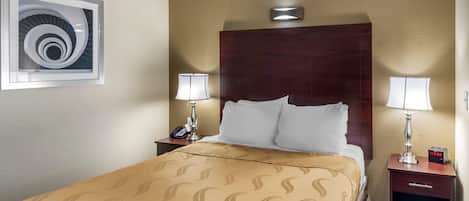 Una habitación de hotel con una cama grande, dos mesitas de noche con lámparas, un reloj y una obra de arte colgada en la pared.