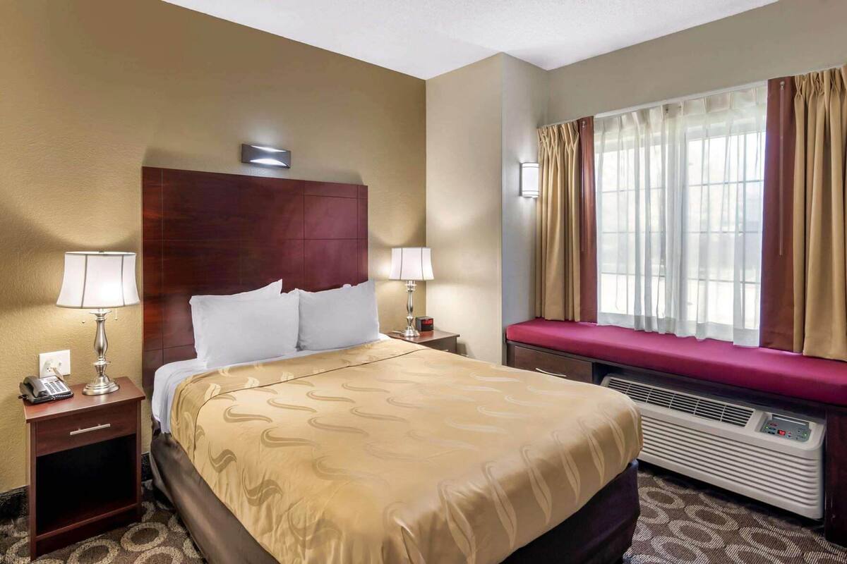 Habitación de hotel con una cama grande, lámparas de noche, un calentador y una ventana con cortinas.