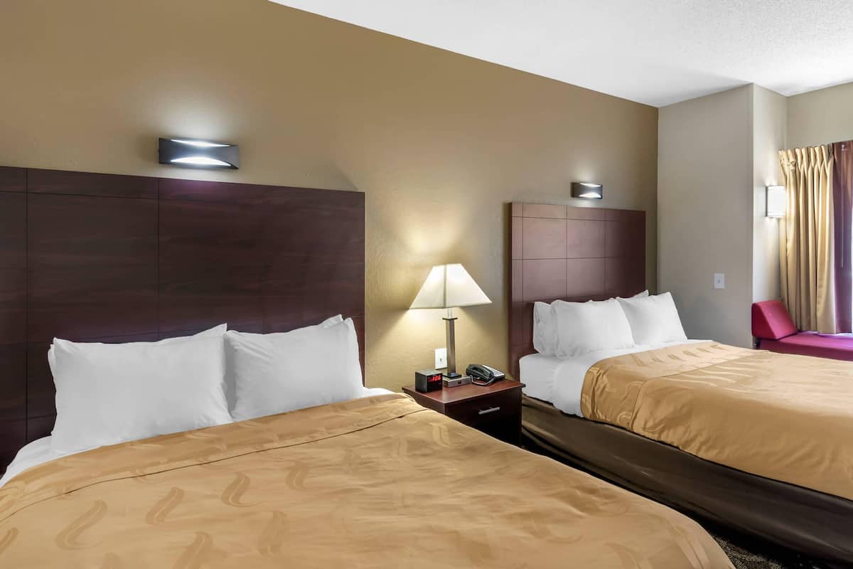 Habitación de hotel con dos camas, una mesita de noche con lámpara, teléfono y reloj.