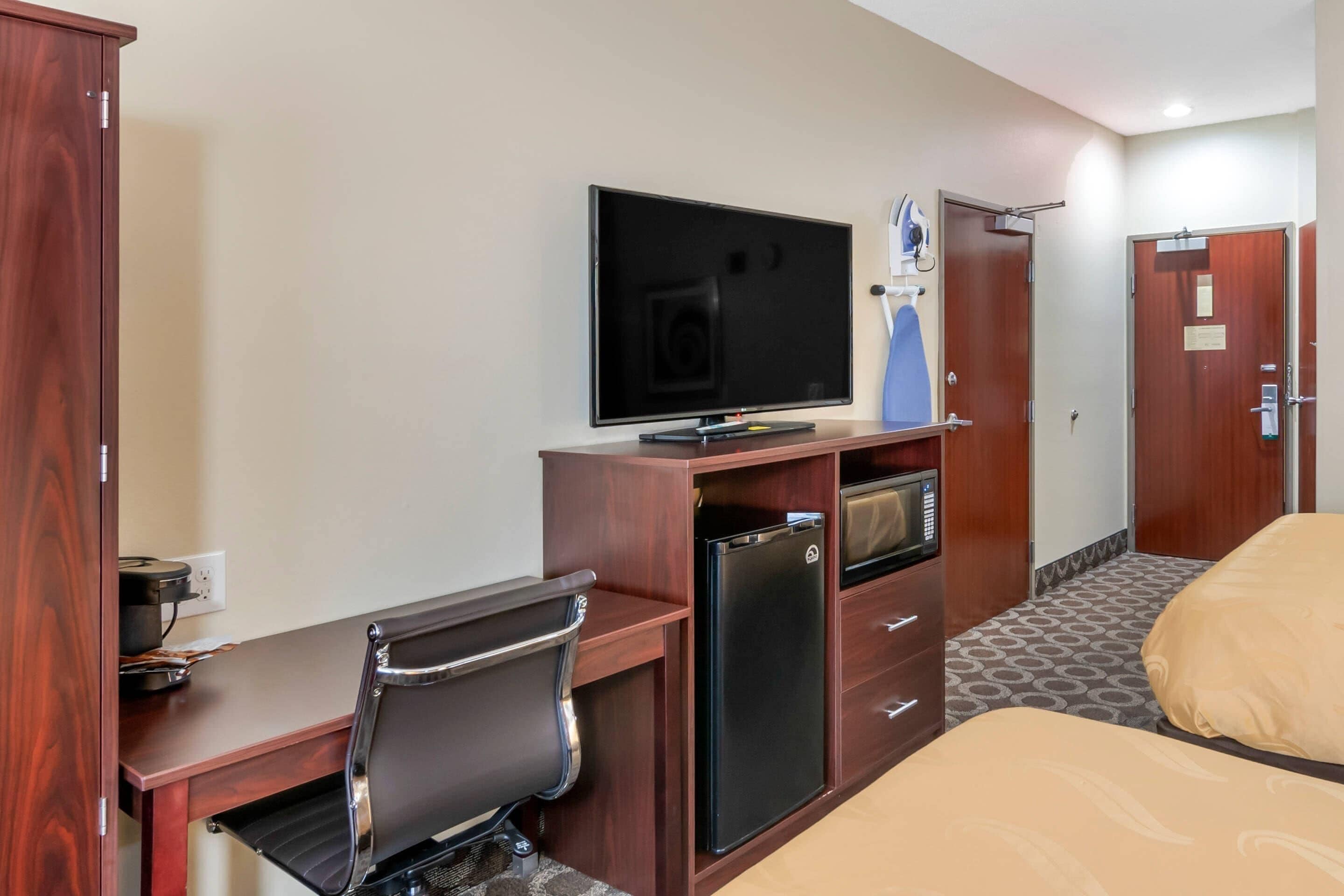Quarto de hotel com escrivaninha, cadeira, televisão, minibar e uma cama.