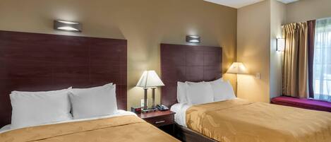 Una habitación de hotel con dos camas, una mesita de noche con lámpara, una ventana con cortinas y un aplique de pared.