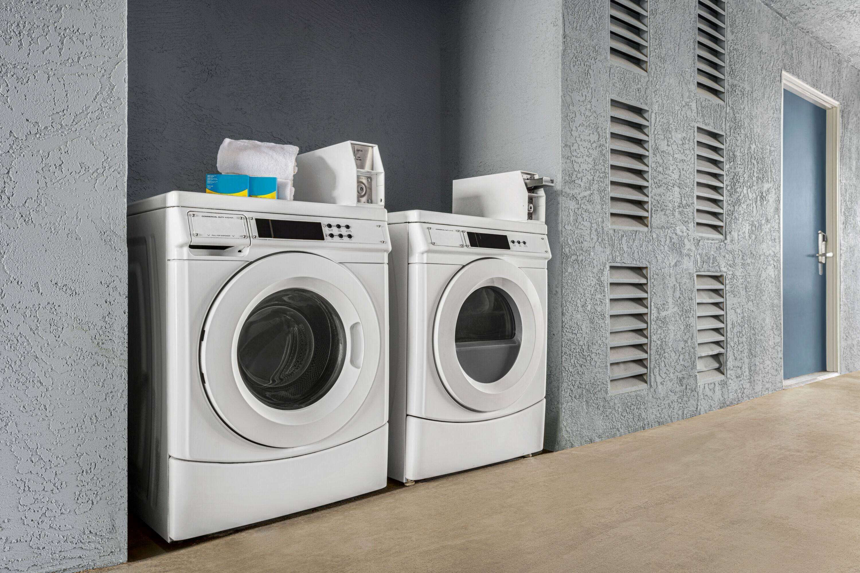 Two front-loading washing machines in a laundry room with a grey textured wall and a blue door.