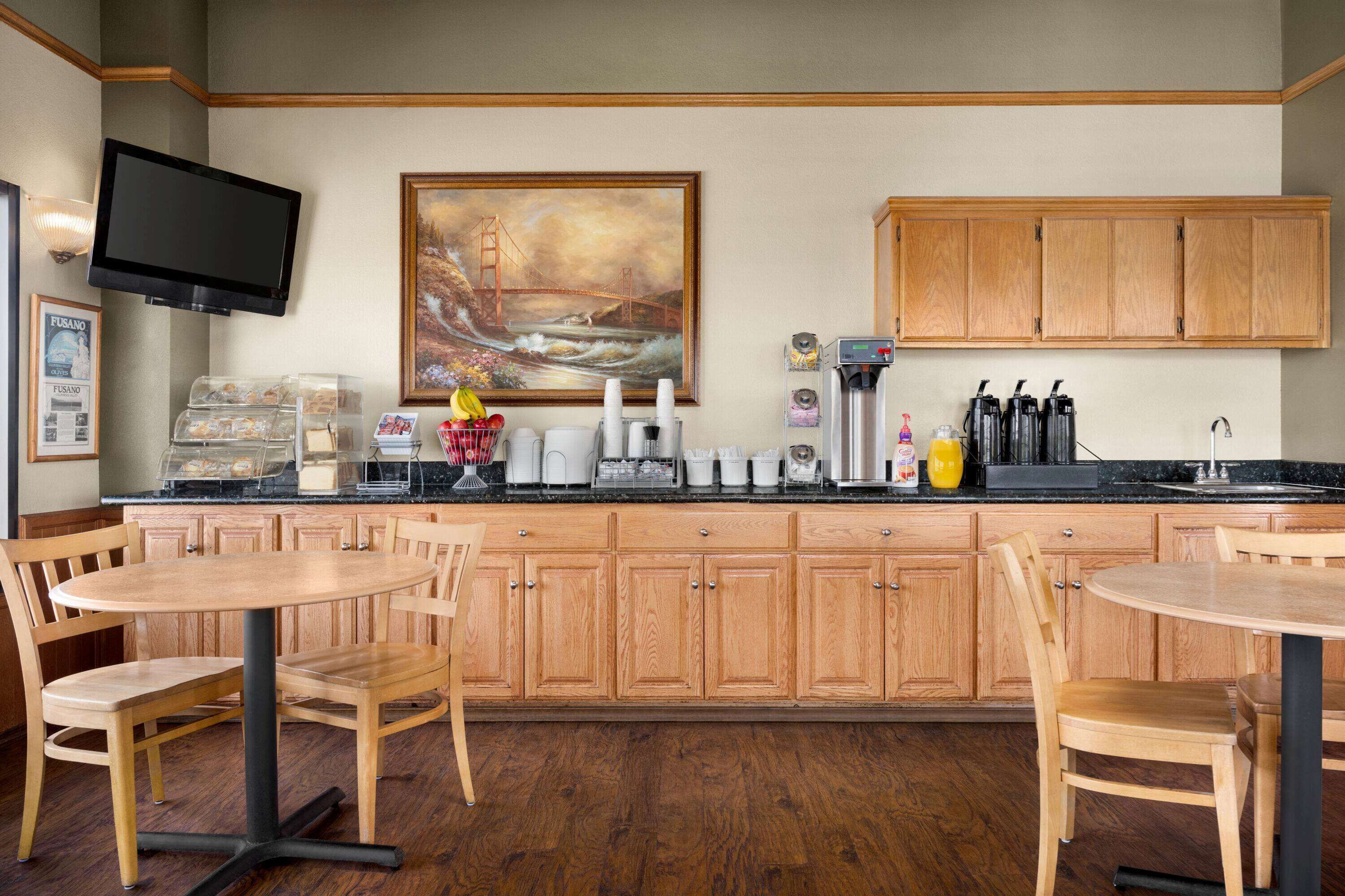 A kitchen with wooden cabinets, a TV mounted on the wall, and a painting of a bridge.
