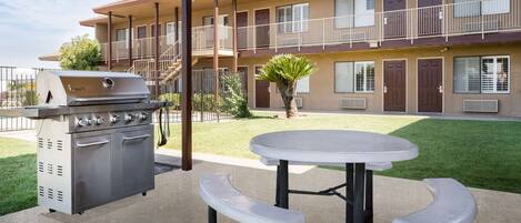 A patio with a barbecue grill, a round table, and two benches.