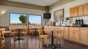 A kitchen with wooden cabinets, a dining area with a round table and chairs, a television mounted on the wall, and a view of the outdoors through large windows. - Super 8 by Wyndham Lindsay Olive Tree (Lindsay)