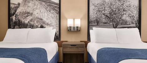 A hotel room with two beds, a nightstand with a lamp, and two framed pictures on the wall.