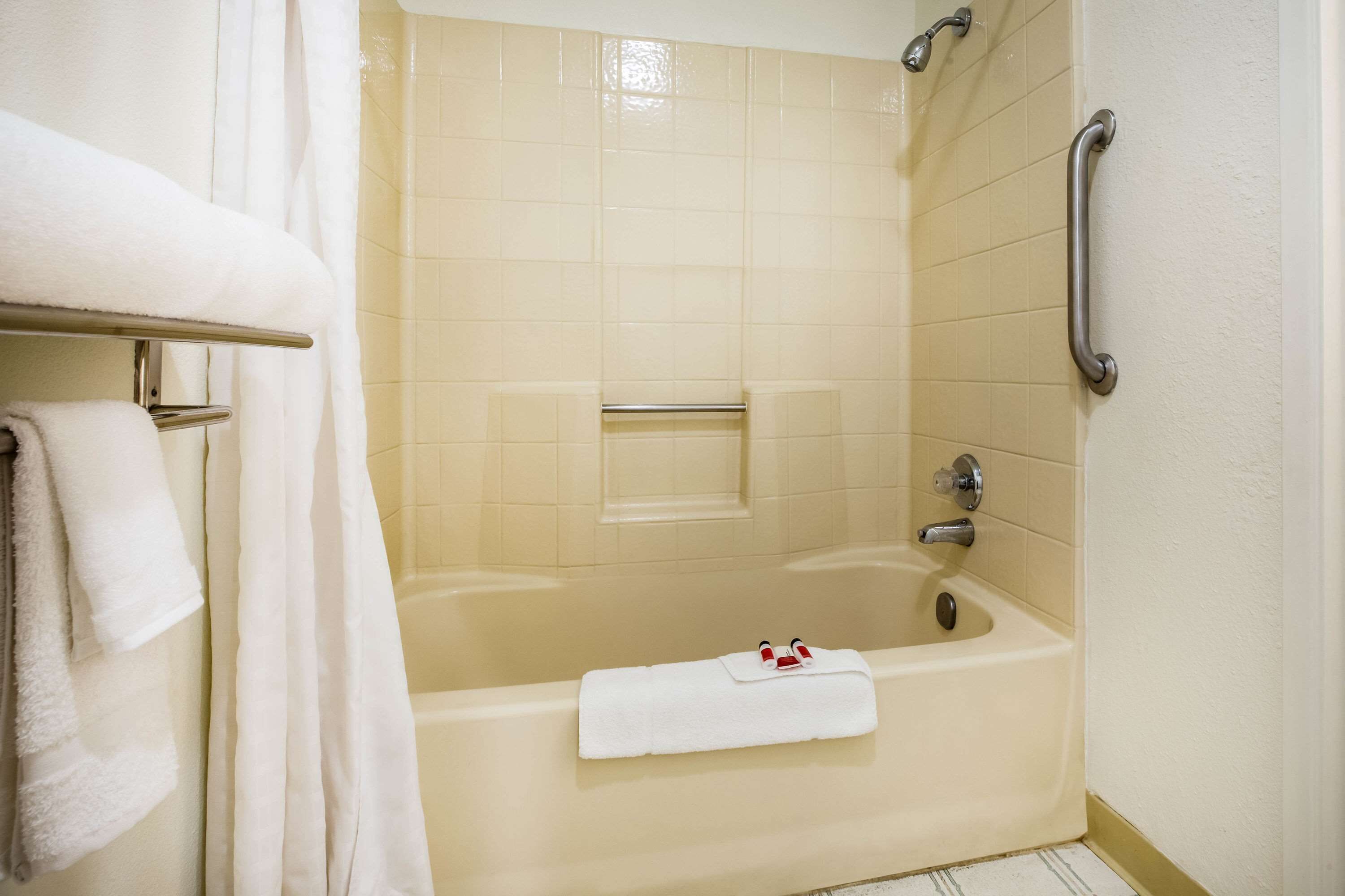 A bathroom with a bathtub, a handrail, and a towel rack with towels.