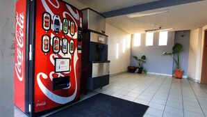 A Coca-Cola vending machine in a hallway with tiled flooring, potted plants, and a security camera on the ceiling. - Americas Best Value Inn Moline (Moline)