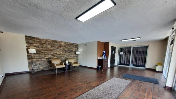 A spacious lobby with a stone wall, two leather chairs, a small table, and a reception desk. - Americas Best Value Inn Moline (Moline)