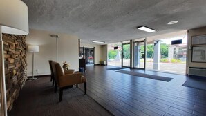 A spacious lobby with a stone wall, a chair, a floor lamp, and a view of the outside parking area. - Americas Best Value Inn Moline (Moline)