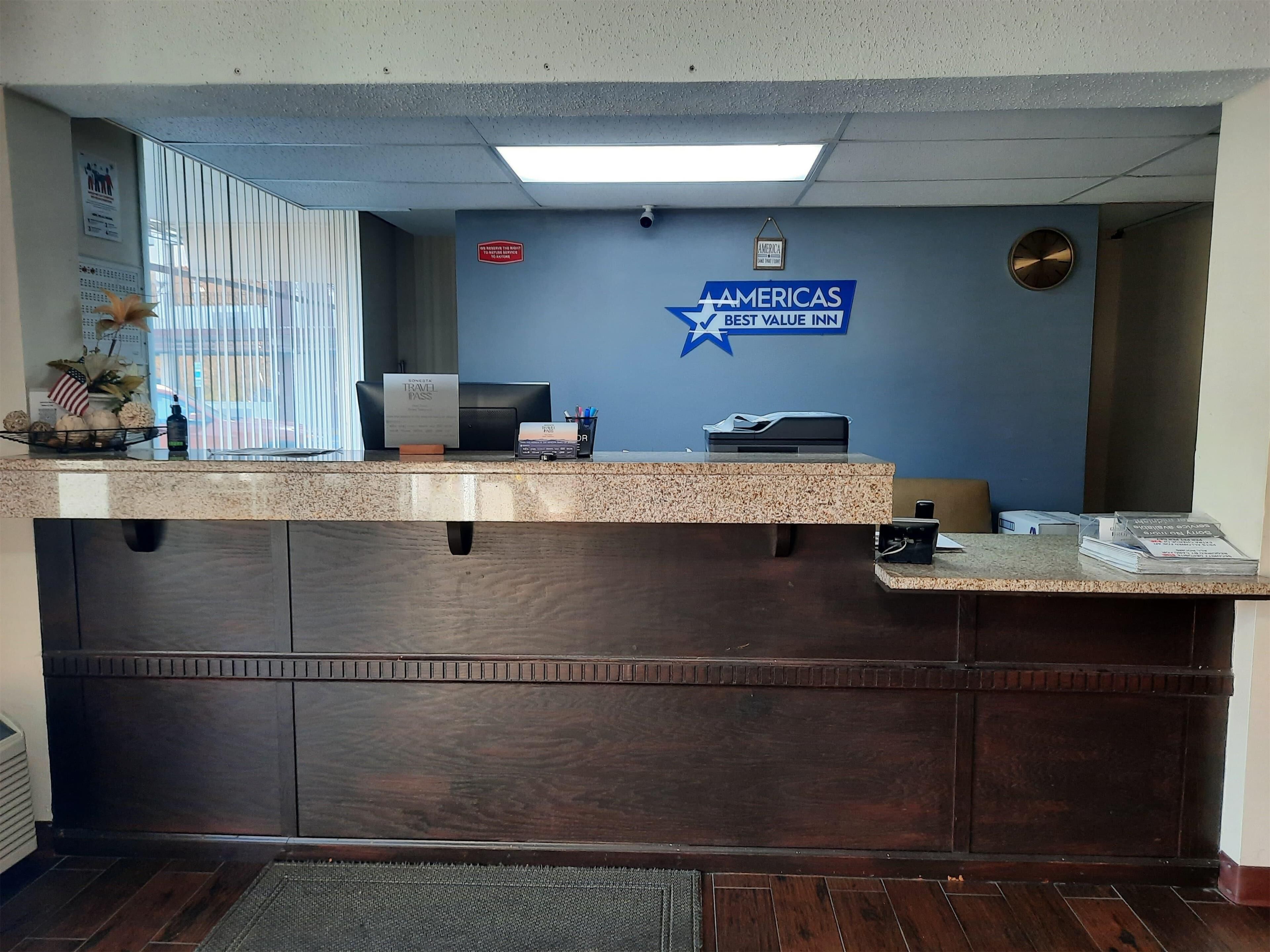 A reception desk with a blue wall, a sign for 'AMERICAS BEST VALUE INN', and a clock.
