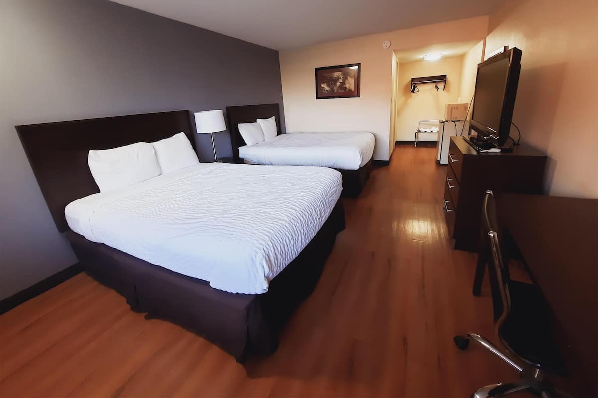 A hotel room with two beds, a desk, a chair, a TV, and a lamp.