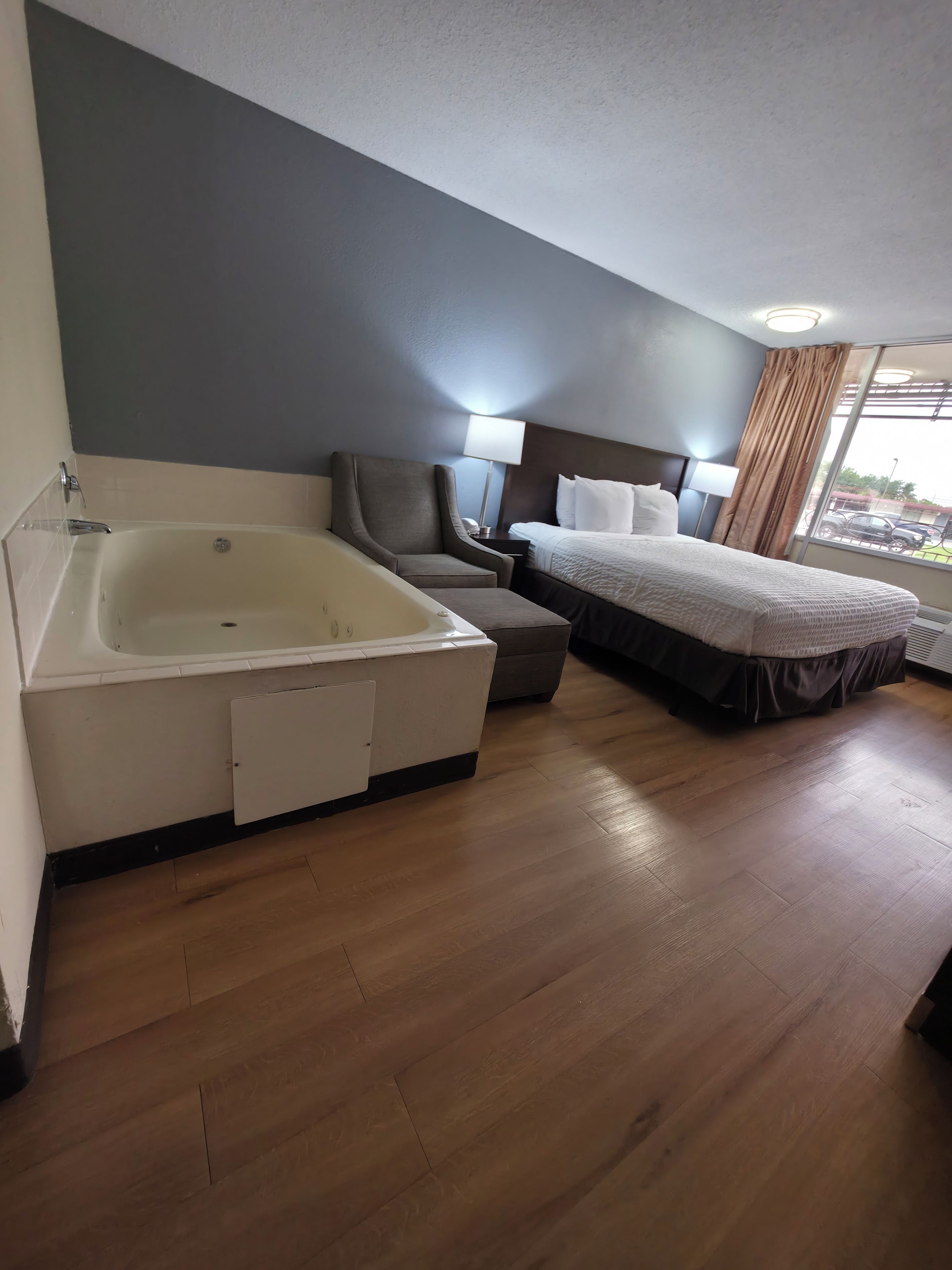 Una habitación de hotel con bañera, cama, sillón y ventana con cortinas.
