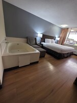 Una habitación de hotel con bañera, cama, sillón y ventana con cortinas.