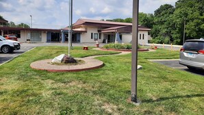 A building with a parking lot, a flagpole with an American flag, and a landscaped area with a rock centerpiece. - Americas Best Value Inn Moline (Moline)