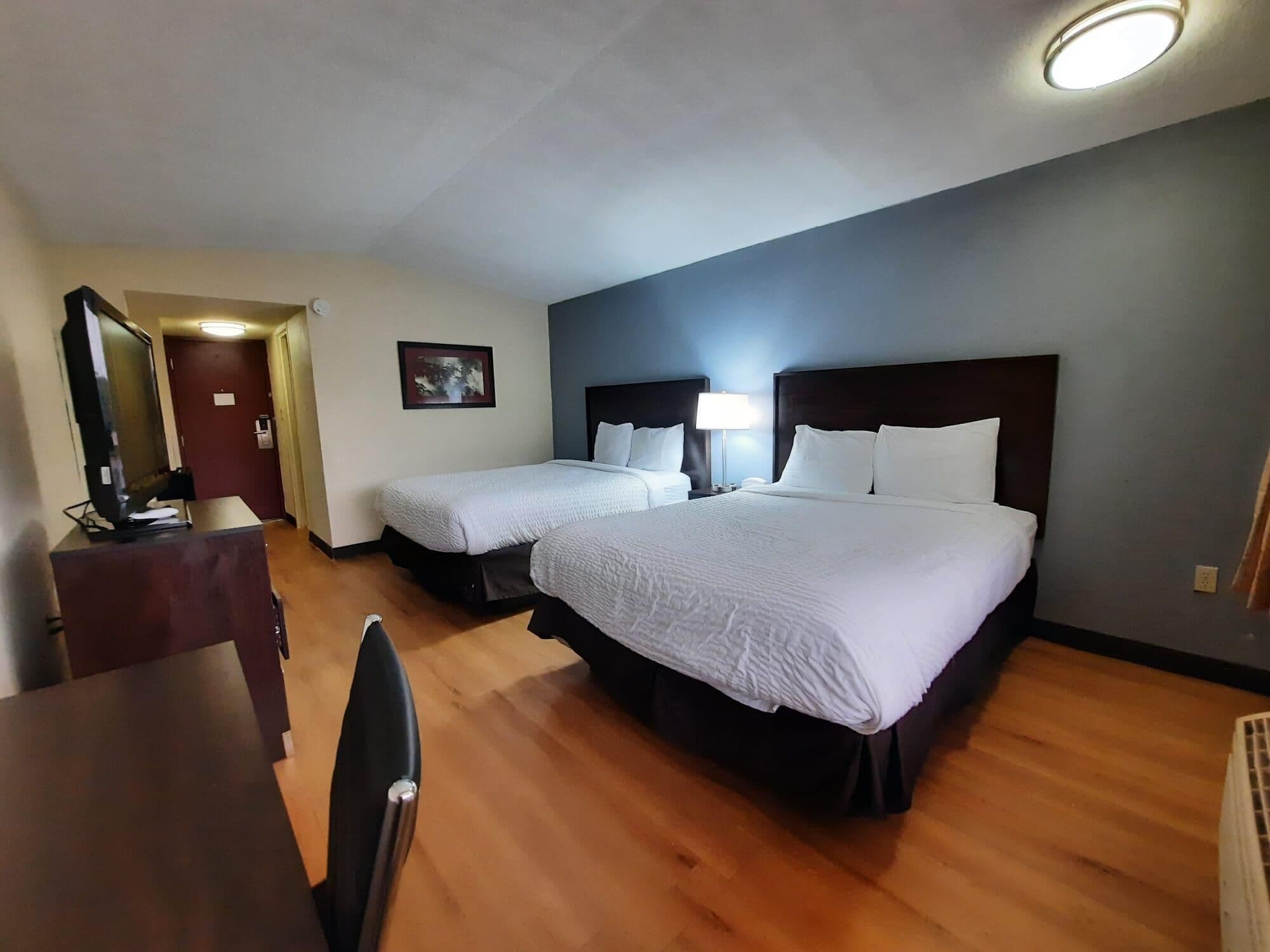 A hotel room with two beds, a desk, a chair, a television, and a framed picture on the wall.