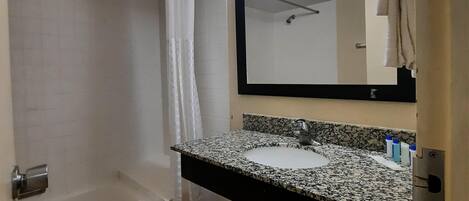 A bathroom with a bathtub, a sink with a granite countertop, a mirror, and a shower curtain.